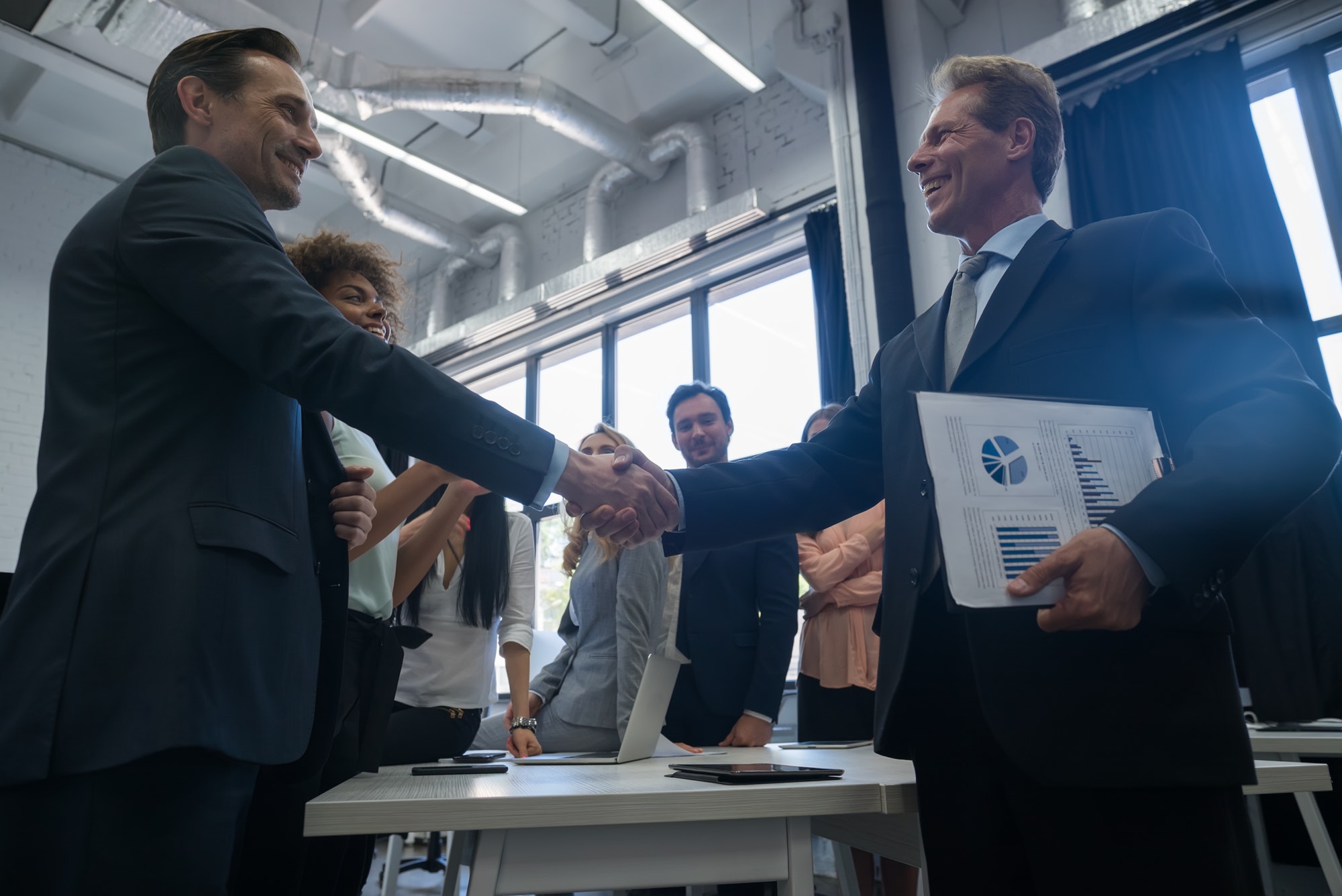 Business Handshake With Businesspeople On Background, Colleagues Shaking Hands During Meeting After